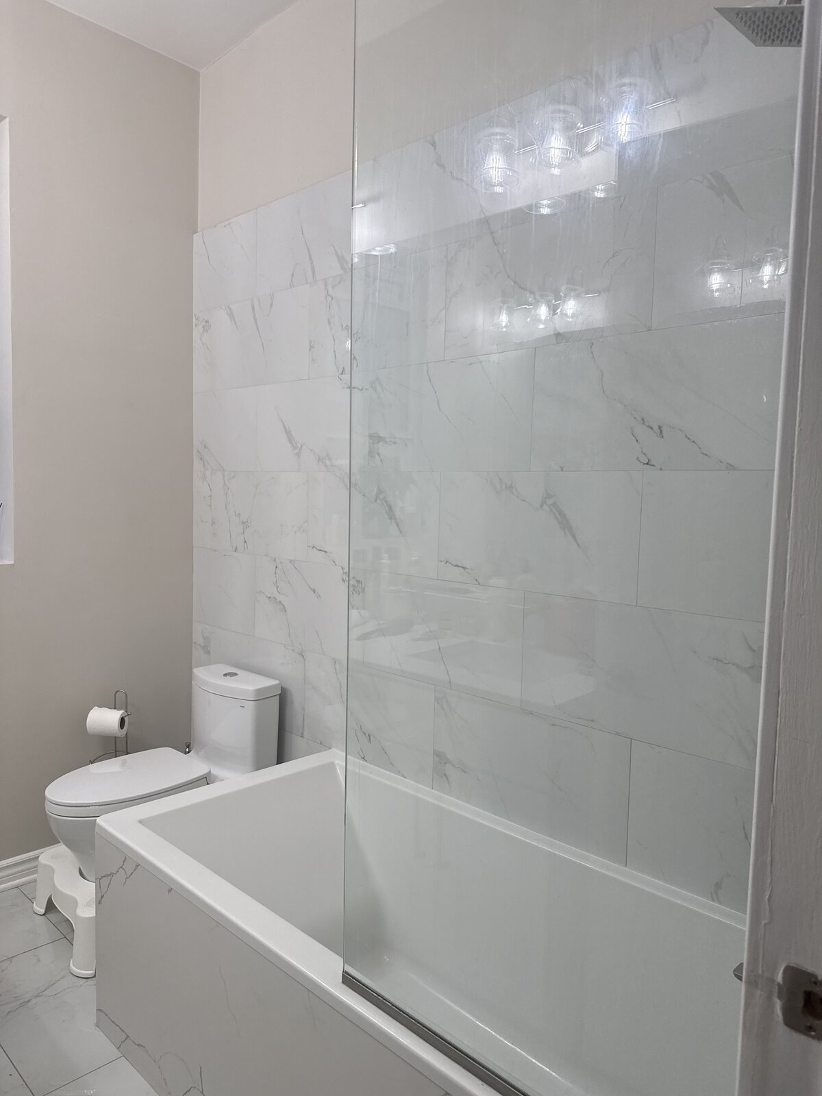 Remodeled bathroom with marble-look tile and frameless glass shower divider